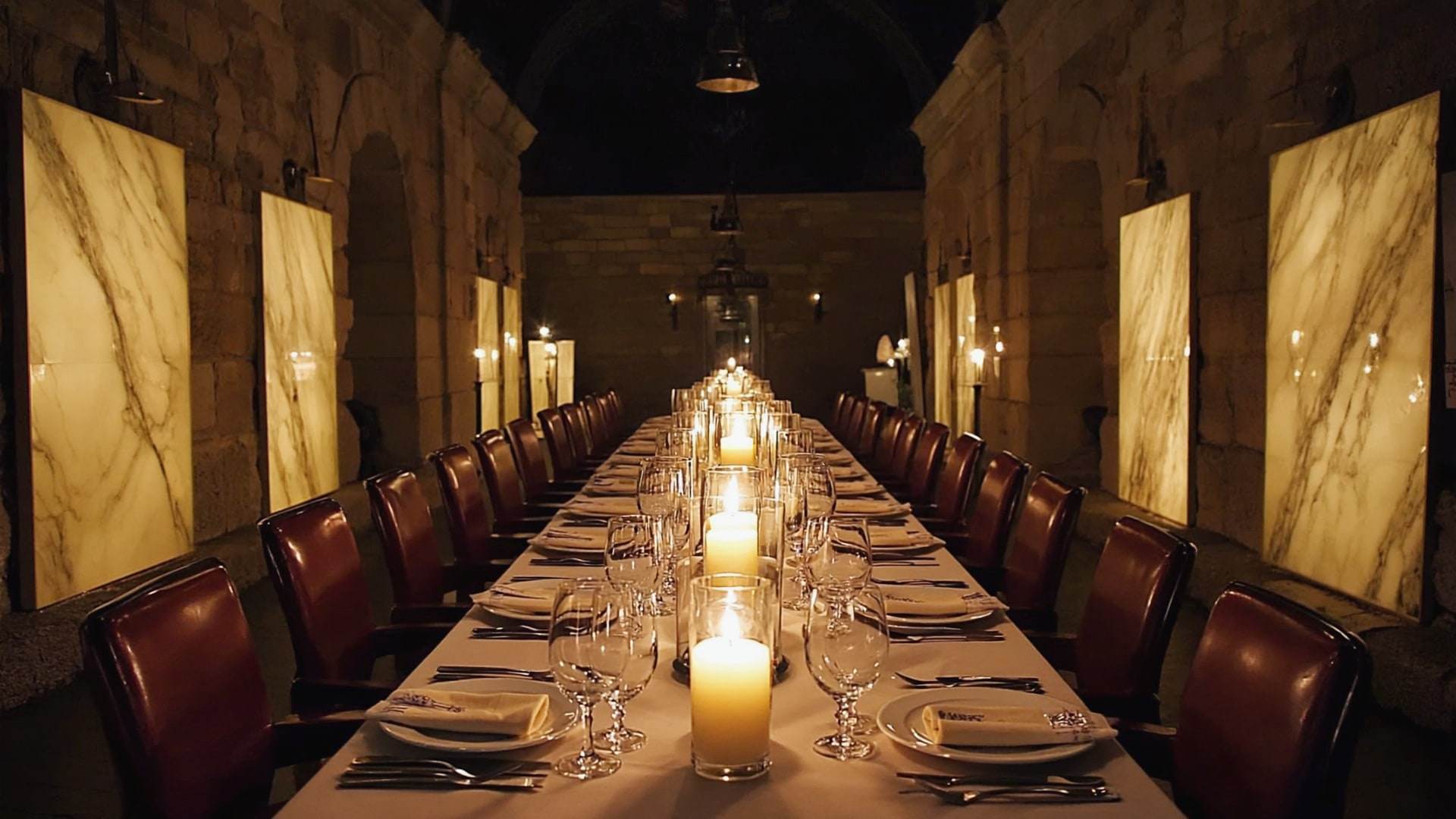 A long candlelit table set for a private dinner inside a stone gallery.