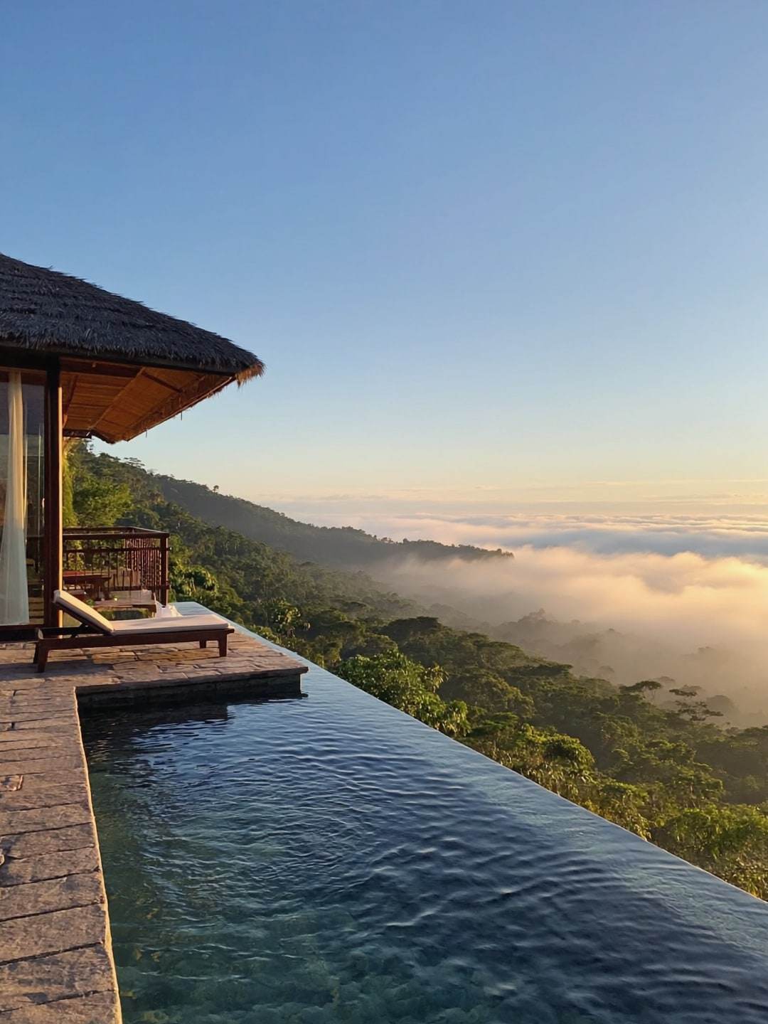 An infinity-edge pool terrace above a misty rainforest valley at golden hour.