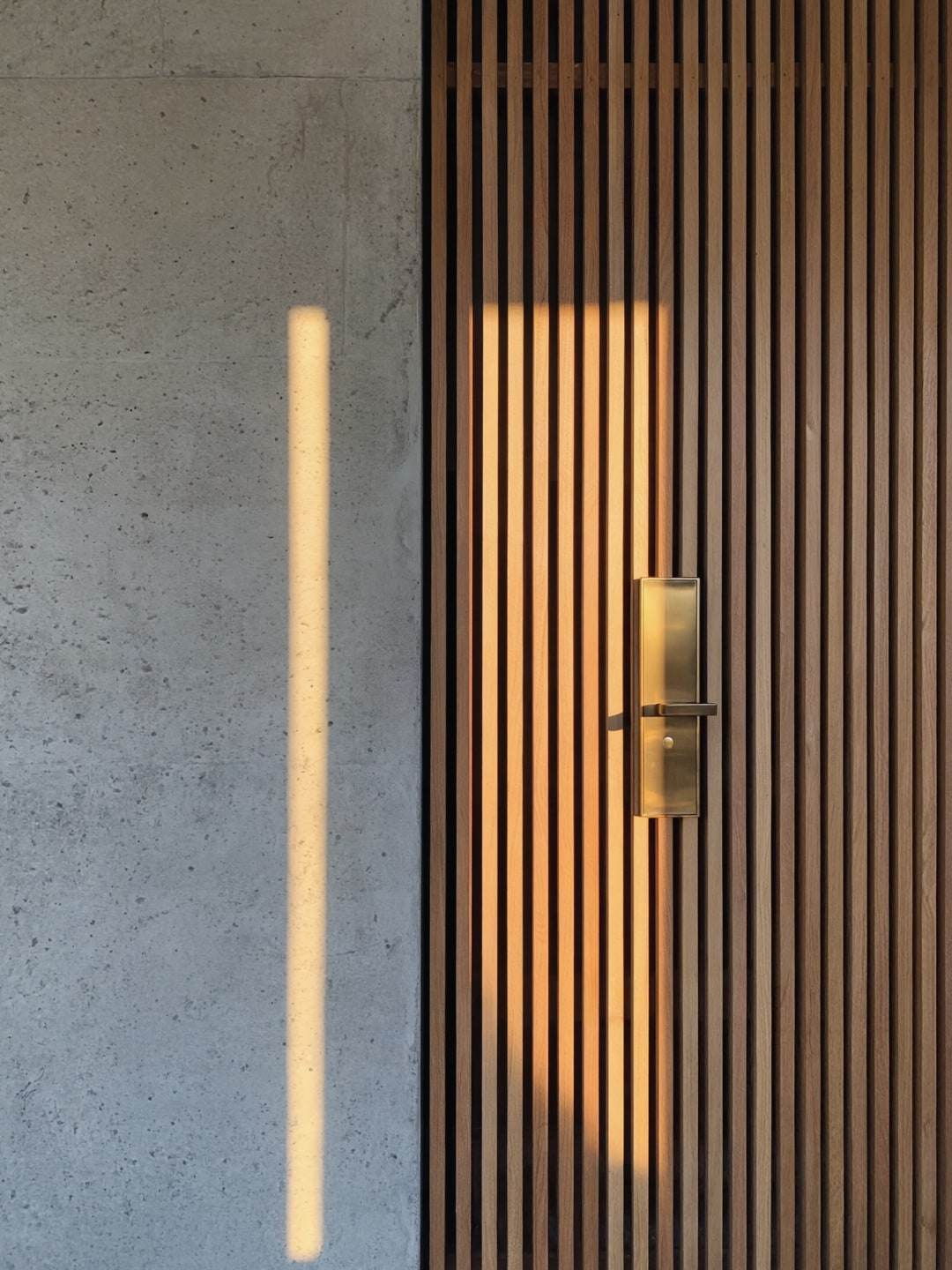 Konkrit bertekstur papan bersebelahan skrin bilah jati dan pemegang pintu gangsa.